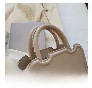 Detail of cream designer bag featuring wave-edge design and rounded ergonomic handles