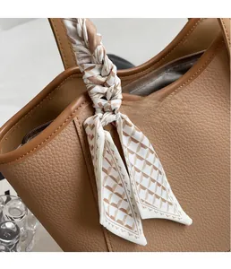 Detail of a brown lychee leather tote bag handle wrapped with a geometric silk scarf