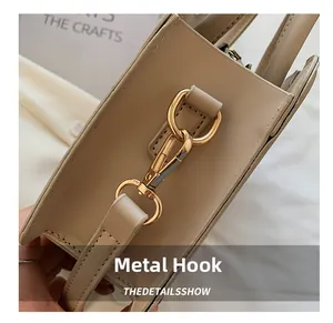 Close-up of golden metal hook hardware and rotating clasp on a beige textured handbag