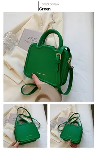 Close-up of green leather handbag with gold lettering and unique top handle design