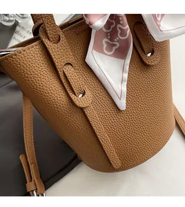 Close-up of brown pebbled leather bucket bag featuring a decorative patterned silk scarf