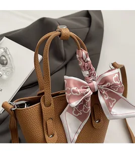 Detail of a brown lychee leather handbag with a pink floral silk scarf tied to the handle