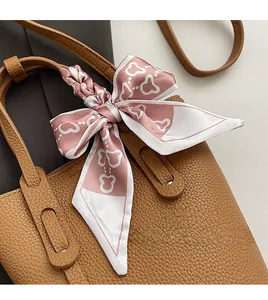 Close-up of pink silk heart pattern scarf tied in a bow on a brown leather handbag handle