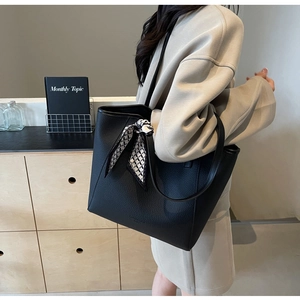 Detail of black lychee grain leather tote bag with decorative silk scarf on shoulder strap