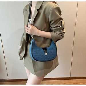 Chic blue denim moon bag with black leather trim worn by model in green suit
