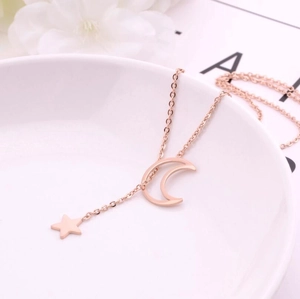 Close-up of rose gold star and moon pendant necklace on a white ceramic tray