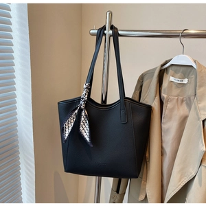 Detail of black pebbled leather tote bag with decorative scarf on a metal display stand
