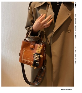 Close-up of vintage brown leather bucket bag with printed strap and rabbit doll charm