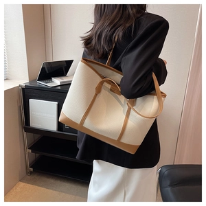 Detailed side view of a large cream and brown leather tote bag worn by a model