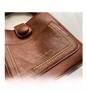 Detail of Mandan Verse logo on vintage brown leather bucket bag with visible grain texture
