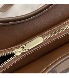 Detailed close-up of golden metal zipper and contrast white stitching on brown leather bag