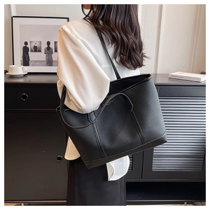 Detail of black pebbled leather tote bag worn on shoulder by a model in a minimal setting