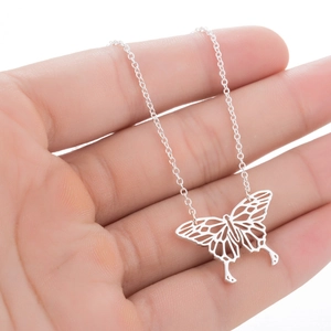 Vue macro d'un pendentif papillon argenté ajouré sur une fine chaîne en main