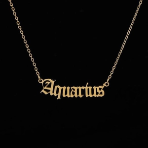 Macro view of gold Aquarius zodiac pendant with gothic font and delicate link chain