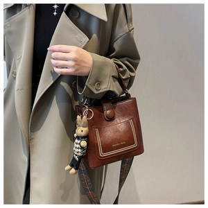 Detail of dark brown bucket bag with plush bunny charm and retro patterned shoulder strap