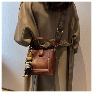 Detail of dark brown leather bucket bag with wide woven strap and rabbit charm accessory