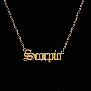 Close-up of golden Scorpio necklace with vintage Gothic lettering on black background