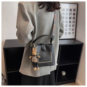 Detail of black bucket bag with gold studs, brand logo, and woven ethnic strap