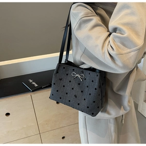 Detail of grey bucket bag with embroidered bows and metallic bow charm in model context