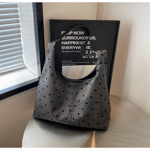 Detailed view of gray polka dot canvas tote bag with black bow on a metallic table