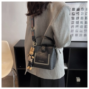 Detail of black leather bucket bag with wide printed strap and cute rabbit pendant charm