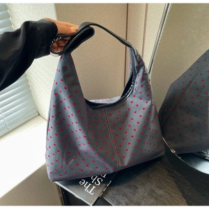 Detail of grey canvas tote bag featuring red heart patterns and black leather handles