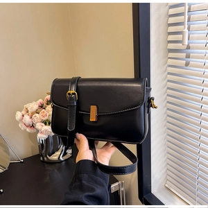 Close-up of black leather crossbody bag featuring a vintage gold rectangular buckle