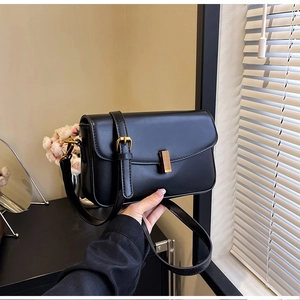 Close-up of black leather crossbody bag featuring a golden rectangular metal clasp