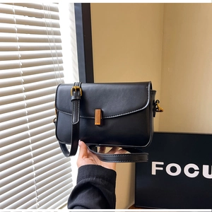Detail of black faux leather crossbody bag with gold rectangular clasp and focus branding