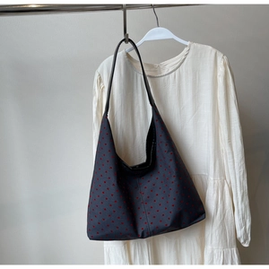 Detail of a large black canvas tote bag with red heart pattern hanging on a white dress