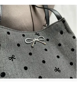 Detail view of gray herringbone fabric with black velvet dots and metal bow pendant