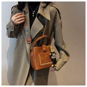 Brown vintage bucket bag with patterned strap and rabbit charm shown on a model
