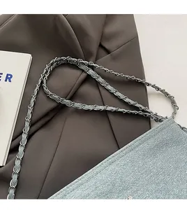 Detail of light blue denim bucket bag with woven silver metal chain and fabric strap