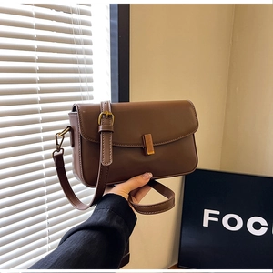 Detail of a brown leather crossbody bag featuring a gold square buckle and white stitching
