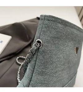 Close-up of blue denim woven bucket bag featuring metallic chain and triangular plaque