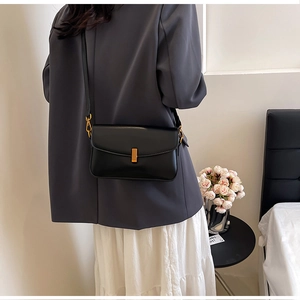Close-up of a black minimalist underarm bag featuring a golden metallic buckle detail