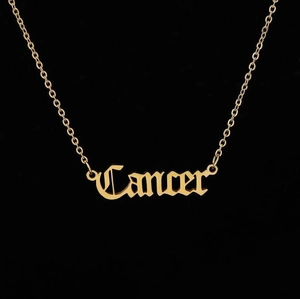 Close-up of gold gothic Cancer necklace with a delicate cable chain on black background