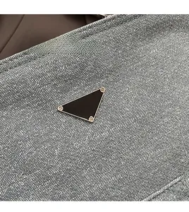 Close-up of the triangular metal emblem on gray denim fabric with gold hardware details