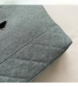 Close-up of quilted grey denim fabric with a black triangular logo on a bucket bag