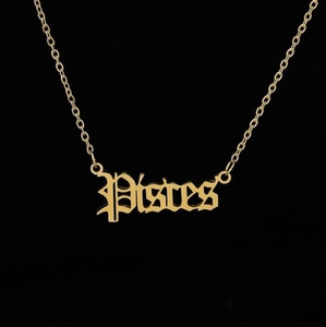 Close-up of gold Pisces zodiac pendant with gothic lettering and a delicate chain