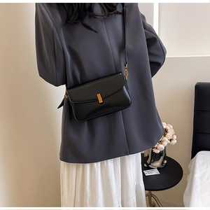 Close-up of black leather crossbody bag with elegant rectangular gold metal lock detail
