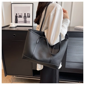 Close-up of black lychee grain leather tote bag with reinforced edges and gold logo detail