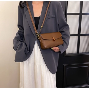 Detail of brown leather crossbody bag with golden buckle on a fashion model