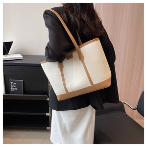 Close-up of beige tote bag with litchi texture and brown leather trim on shoulder