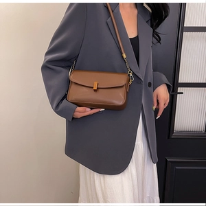 Detail of a brown leather crossbody bag with gold buckle on a model in a grey blazer