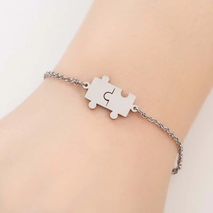 Detail of silver puzzle piece pendant on a stainless steel chain worn on the wrist