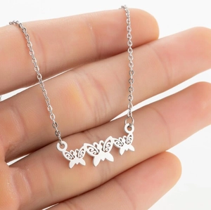 Detail view of a silver necklace with three intricate hollow butterfly charms held by hand