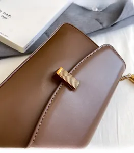 Gros plan du sac bandoulière en cuir marron avec une boucle en métal doré rectangulaire