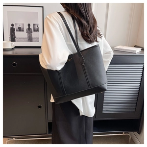 Detail of black lychee texture tote bag featuring a gold logo and long shoulder strap
