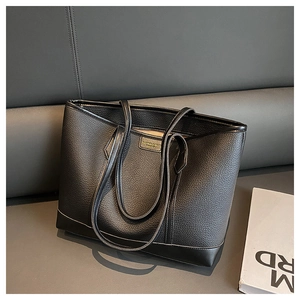 Detail of black lychee grain tote bag with zipper and fashion leather logo on a sofa